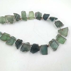 May include: A strand of green and blue gemstone beads strung on silver wire. The beads are irregular in shape and have a rough, natural texture.