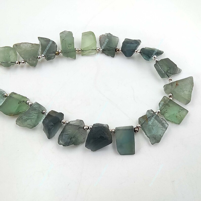May include: A strand of green and blue gemstone beads strung on silver wire. The beads are irregular in shape and have a rough, natural texture.