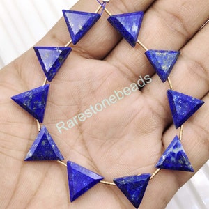 Könnte beinhalten: Eine Strähne aus 12 dreieckigen Lapislazuli-Perlen mit goldfarbenem Draht. Die Perlen sind tiefblau mit goldenen Pyrit-Flocken. Die Perlen sind auf einem goldfarbenen Draht aufgefädelt und bereit für die Schmuckherstellung.