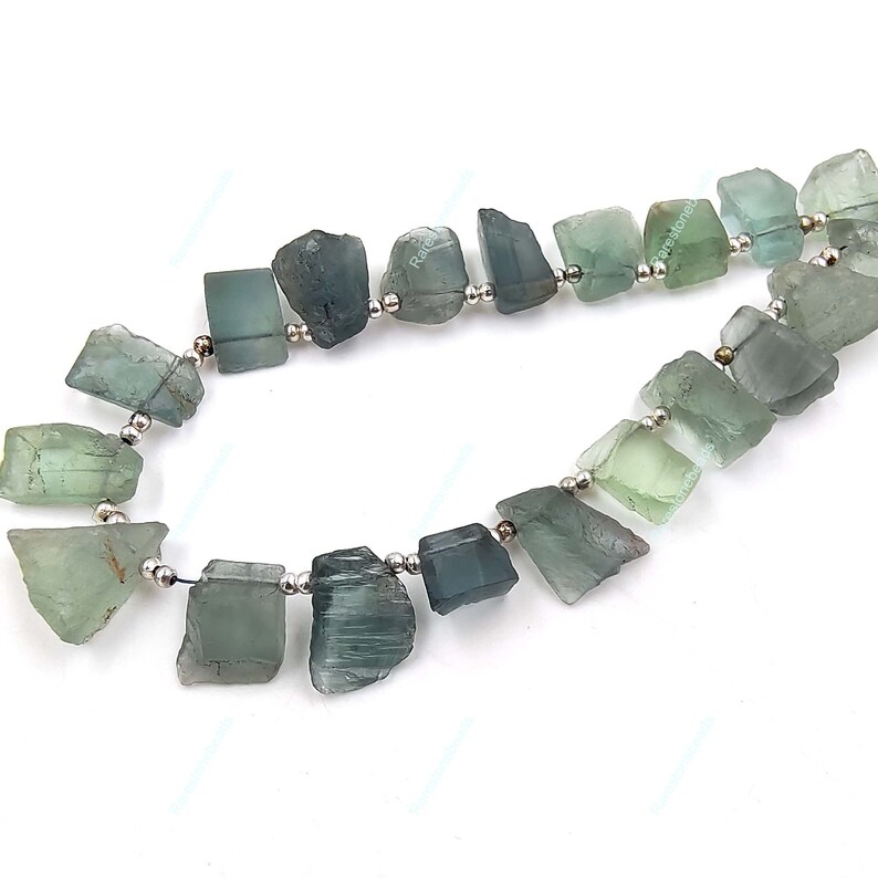 May include: A strand of light blue and green gemstone beads with silver spacers. The beads are irregularly shaped and have a rough, natural look.