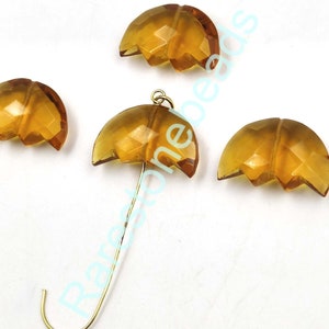 May include: Four amber glass beads in the shape of an umbrella. The beads are faceted and have a shiny finish. One bead is attached to a gold-colored wire.