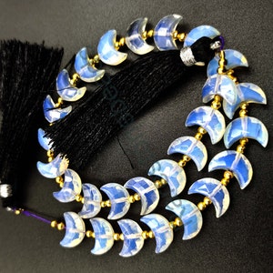 May include: A strand of iridescent opal crescent moon beads with gold spacers. The beads are strung on a purple cord with a black tassel.