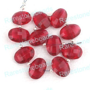 Könnte beinhalten: Eine Strähne roter, facettierter ovaler Edelsteinperlen mit silbernen Zwischenstücken. Die Perlen sind auf einem dünnen Draht aufgefädelt.