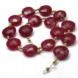May include: A strand of faceted, oval-shaped, deep red gemstone beads. The beads are strung together with gold-colored spacers and wire, creating a necklace or bracelet component. The gemstones have a polished, reflective surface.