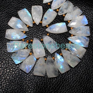 Könnte beinhalten: Eine Strähne aus irisierenden weißen Mondsteinperlen in Tropfenform. Die Perlen sind auf einem Draht mit goldfarbenen Zwischenstücken aufgefädelt.