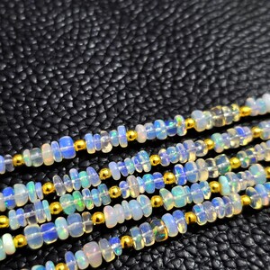 May include: Close-up of multiple strands of beaded necklaces. The necklaces feature small, irregular-shaped opalescent beads with flashes of blue, green, and yellow. Gold-colored beads are interspersed between the opalescent beads.