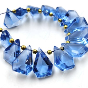 May include: A strand of blue gemstone beads with gold accents. The beads are faceted and have a teardrop shape. The beads are strung on a thin wire.