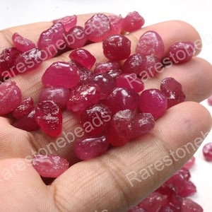 Könnte beinhalten: Nahaufnahme einer Hand, die einen Haufen loser, facettierter Rubin-Edelsteine hält. Die Rubine sind tiefrot und haben verschiedene Formen und Größen.