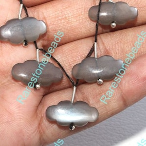 May include: A strand of grey gemstone beads in the shape of clouds, strung on black thread with silver accents.
