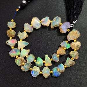 May include: A strand of iridescent opal gemstone beads, each with a unique shape and color variation. The beads are strung on a gold-colored wire with small gold beads between each opal bead.