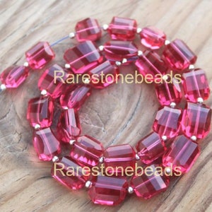 May include: A strand of pink faceted crystal beads strung on silver wire. The beads are rectangular in shape and have a slight shimmer. The beads are arranged in a circular pattern, with the ends of the strand meeting in the centre.