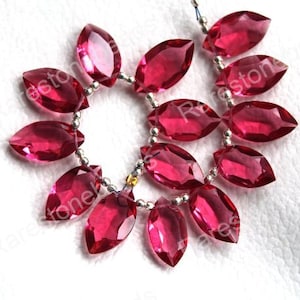 May include: Strand of faceted, oval-shaped, deep pink gemstones strung on a silver-colored wire. The gemstones are arranged in a circular pattern, with each stone reflecting light. The beads are approximately 1 inch in length.