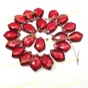 May include: Strand of faceted, deep red gemstone beads with gold-colored spacers. The beads are irregularly shaped with multiple facets, catching the light. The text "Rarestonebeads" is printed on the image.