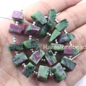 以下が含まれることがあります： 緑とピンクの宝石ビーズとシルバーのスペーサーがついたビーズのストランド。ビーズはファセットカットされており、長方形の形をしています。ビーズはシルバーワイヤーに糸で通されています。