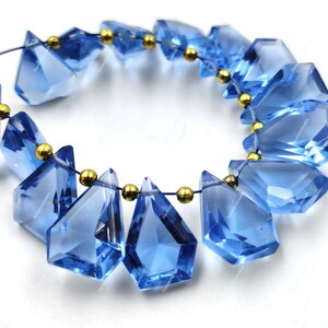 May include: A strand of blue gemstone beads with gold accents. The beads are faceted and have a teardrop shape. The beads are strung on a thin wire.