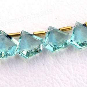 Puede incluir: Una hebra de cuentas de piedra preciosa facetada de color azul claro separadas por espaciadores dorados. Las cuentas tienen forma de diamante con una parte superior puntiaguda y una parte inferior plana.