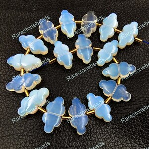 Pode incluir: Um fio de 14 contas de opala azul claro em forma de borboleta com espaçadores dourados. As contas são enfiadas em um fio dourado.