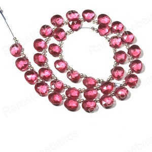 May include: A strand of pink faceted gemstone beads strung on silver wire. The beads are approximately 10mm in diameter and have a faceted, slightly irregular shape.