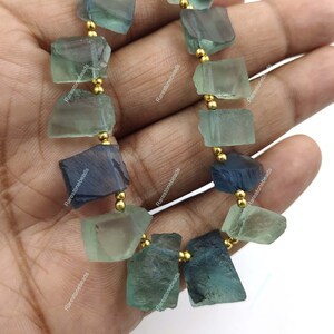 May include: A strand of green and blue faceted gemstone beads with gold spacers. The beads are irregular in shape and have a natural, rough look.
