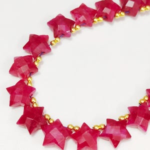 May include: A strand of star-shaped ruby beads strung on a gold wire. The beads are a deep red color and have a faceted finish.