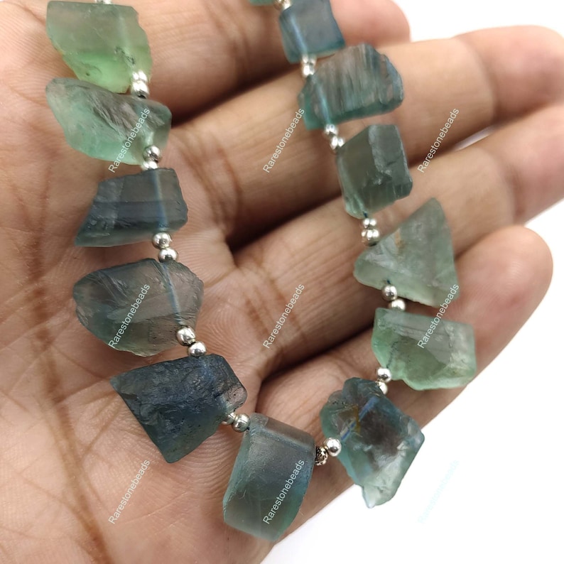 May include: A strand of green and blue fluorite gemstone beads strung on silver wire. The beads are irregular in shape and have a natural, rough texture.