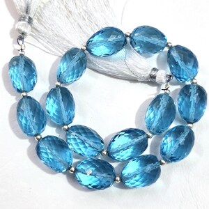May include: A strand of faceted, oval-shaped, light blue gemstones. The beads are strung together with silver-colored metal beads and a white tassel. The gemstones have a translucent quality, reflecting light.
