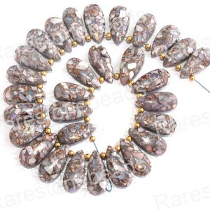 Może przedstawiać: Szereg iryzujących koralików z opalu w kształcie łzy. Koraliki są połączeniem brązu, bieli i szarości z mieniącym się wykończeniem.