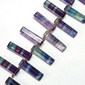May include: A strand of purple, green, and blue fluorite gemstone beads with gold spacers. The beads are rectangular and have a faceted finish.