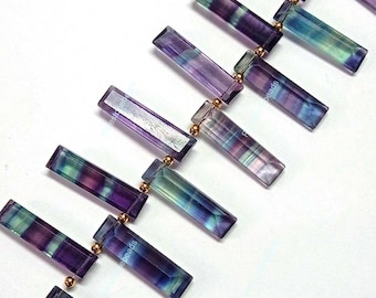 May include: A strand of purple, green, and blue fluorite gemstone beads with gold spacers. The beads are rectangular and have a faceted finish.