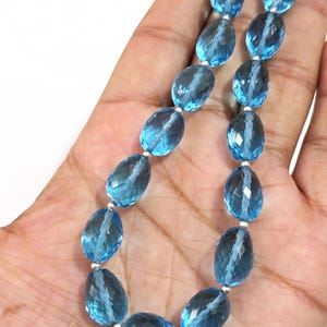 May include: A necklace featuring faceted, oval-shaped blue gemstones strung together with silver-colored beads. The gemstones have a translucent quality, and the necklace is displayed against a neutral background.