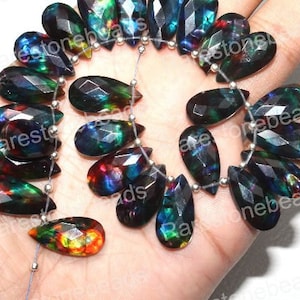 May include: A strand of iridescent black teardrop-shaped gemstone beads. The beads have a rainbow sheen and are strung on a silver wire.