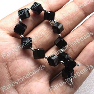 May include: A strand of black gemstone beads, each bead is a cube shape with silver spacers between each bead.