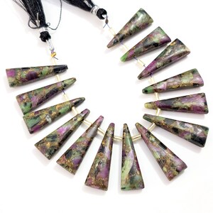 Puede incluir: Un collar de cuentas triangulares de piedras preciosas. Las cuentas son una mezcla de colores verde, morado y dorado. Las cuentas están ensartadas con una borla negra en la parte superior.