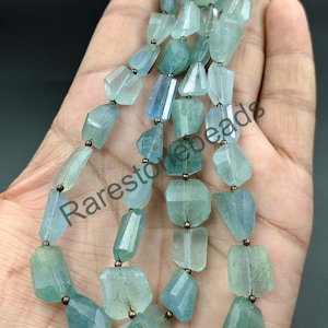 Könnte beinhalten: Eine Strähne aus hellblauen Aquamarin-Edelsteinen mit facettierter, rechteckiger Form. Die Perlen sind auf einem Silberdraht aufgefädelt, mit kleinen Silberperlen zwischen jeder Edelsteinperle. Die Strähne ist etwa 45 cm lang.
