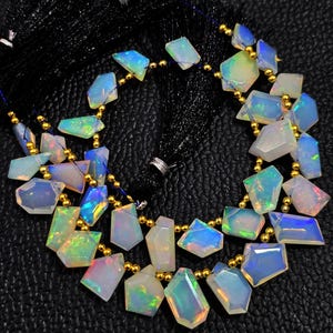 Peut inclure: Un collier composé de pierres précieuses d'opale iridescente de différentes formes géométriques. Les opales sont enfilées avec des perles dorées et un fil bleu foncé. Les pierres précieuses affichent une gamme de couleurs, dont le bleu, le vert et le jaune.