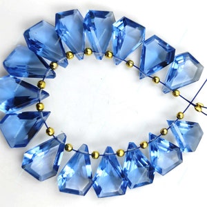 May include: A strand of blue gemstone beads with gold spacers. The beads are faceted and have a teardrop shape. The beads are strung on a clear elastic cord.