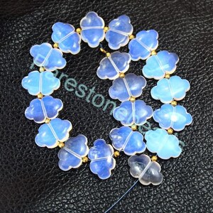 Könnte beinhalten: Eine Kette aus blauen Opal-Edelsteinkugeln in Form eines vierblättrigen Kleeblatts. Die Perlen sind auf einem goldenen Draht aufgefädelt und durch kleine goldene Abstandshalter getrennt.