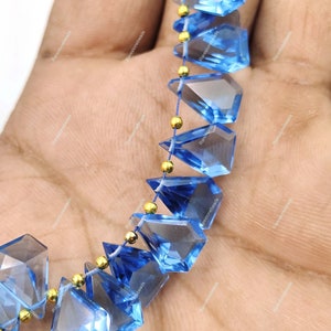 May include: A strand of faceted blue topaz gemstone beads with gold spacers. The beads are faceted in a triangular shape and have a clear, translucent appearance.