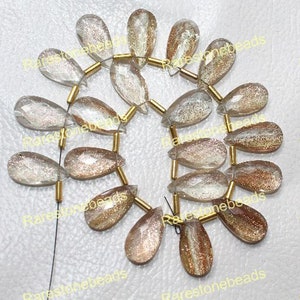 May include: A strand of gold-toned beads with faceted, pear-shaped, translucent, light brown gemstone beads. The beads have a shimmery, iridescent quality.