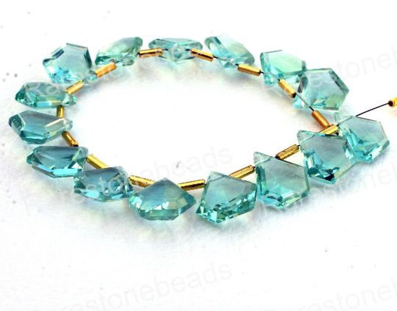 Puede incluir: Una hebra de cuentas de piedras preciosas de color azul claro facetadas con separadores dorados. Las cuentas tienen forma de diamantes y est&aacute;n enhebradas en un alambre.