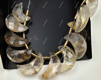 Può includere: Una collana di perle a forma di mezzaluna in quarzo trasparente con inclusiones di rutilo dorato. Le perle sono infilate su un filo d'oro.