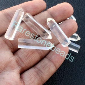 Op de afbeelding: Een verzameling van zes heldere kwartskristalpunten, ook wel toverstokken genoemd, in verschillende maten. De punten zijn glad en gepolijst, met een puntige punt en een platte basis. De kristallen zijn in een hand gerangschikt, met de punten naar boven gericht.