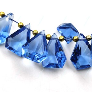 May include: A strand of faceted blue gemstone beads with gold spacers. The beads are teardrop shaped and have a faceted finish.