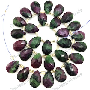 May include: A strand of 20 faceted teardrop-shaped green and pink gemstone beads. The beads are strung on a gold wire with gold spacers between each bead. The beads are approximately 1 inch long.