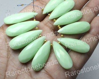 May include: A collection of pale green, teardrop-shaped gemstone beads. Each bead is faceted and strung with gold-colored findings. The beads are displayed against a neutral background, highlighting their color and shape. Ideal for jewelry making.