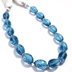 May include: A necklace featuring faceted, oval-shaped, light blue gemstones strung together with silver-colored beads. The necklace is displayed on a white background and has a white tassel at the end.