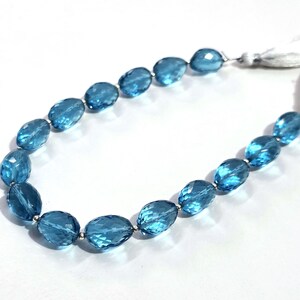 May include: A strand of faceted, oval-shaped blue gemstones, strung together with silver-colored beads. The gemstones are a vibrant, transparent blue. The strand ends with a white tassel.