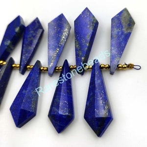 May include: A strand of dark blue lapis lazuli gemstone beads with gold accents. The beads are faceted and have a teardrop shape. The beads are strung on a gold wire.