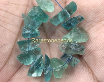 Op de afbeelding: Een streng lichtblauwe en groene fluorite edelsteen kralen, geregen op een blauwe draad. De kralen zijn onregelmatig van vorm en hebben een natuurlijke, ruwe textuur. De kralen zijn ongeveer 1,2 cm groot. Rarestonebeads is afgedrukt op de afbeelding.