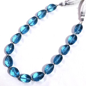 May include: A necklace featuring faceted, oval-shaped blue gemstones strung together with silver-toned metal accents. The necklace has a white tassel closure on each end, creating a delicate and elegant appearance.